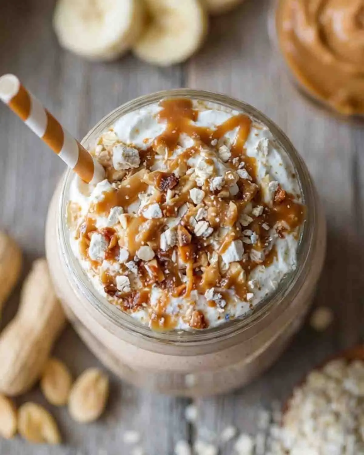 Healthy Protein Peanut Butter Smoothie: Nutty Goodness 3 Healthy protein peanut butter smoothie in a jar topped with whipped yogurt, peanut butter drizzle, oats, and nuts, with banana slices in the background