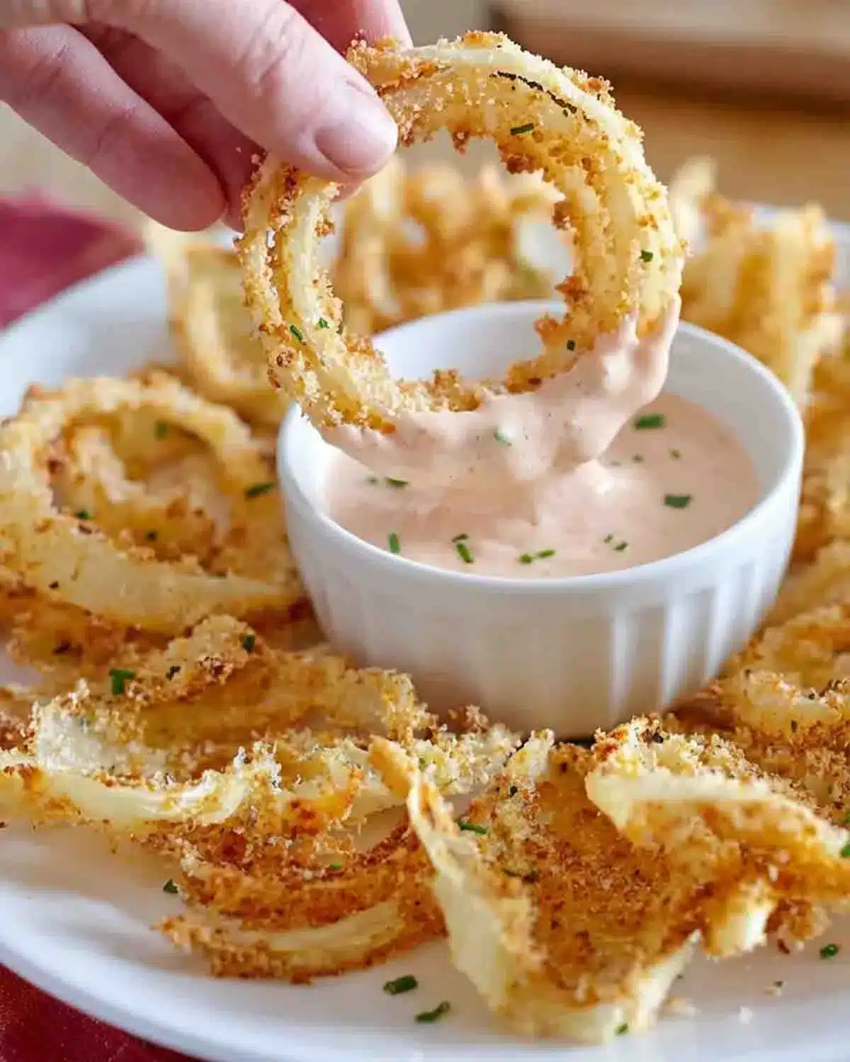 Air-Fryer Crispy Onion Petals 4 Air-Fryer Crispy Onion Petals being dipped into a creamy sauce, showing a close-up of the golden, crunchy coating and tender onion layers.