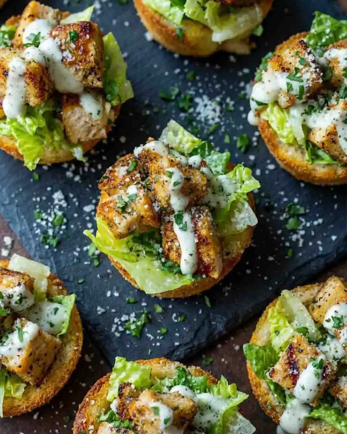 Chicken Caesar Crouton Cups 3 Chicken Caesar Crouton Cups topped with grilled chicken, romaine lettuce, Parmesan, and creamy Caesar dressing on a serving platter