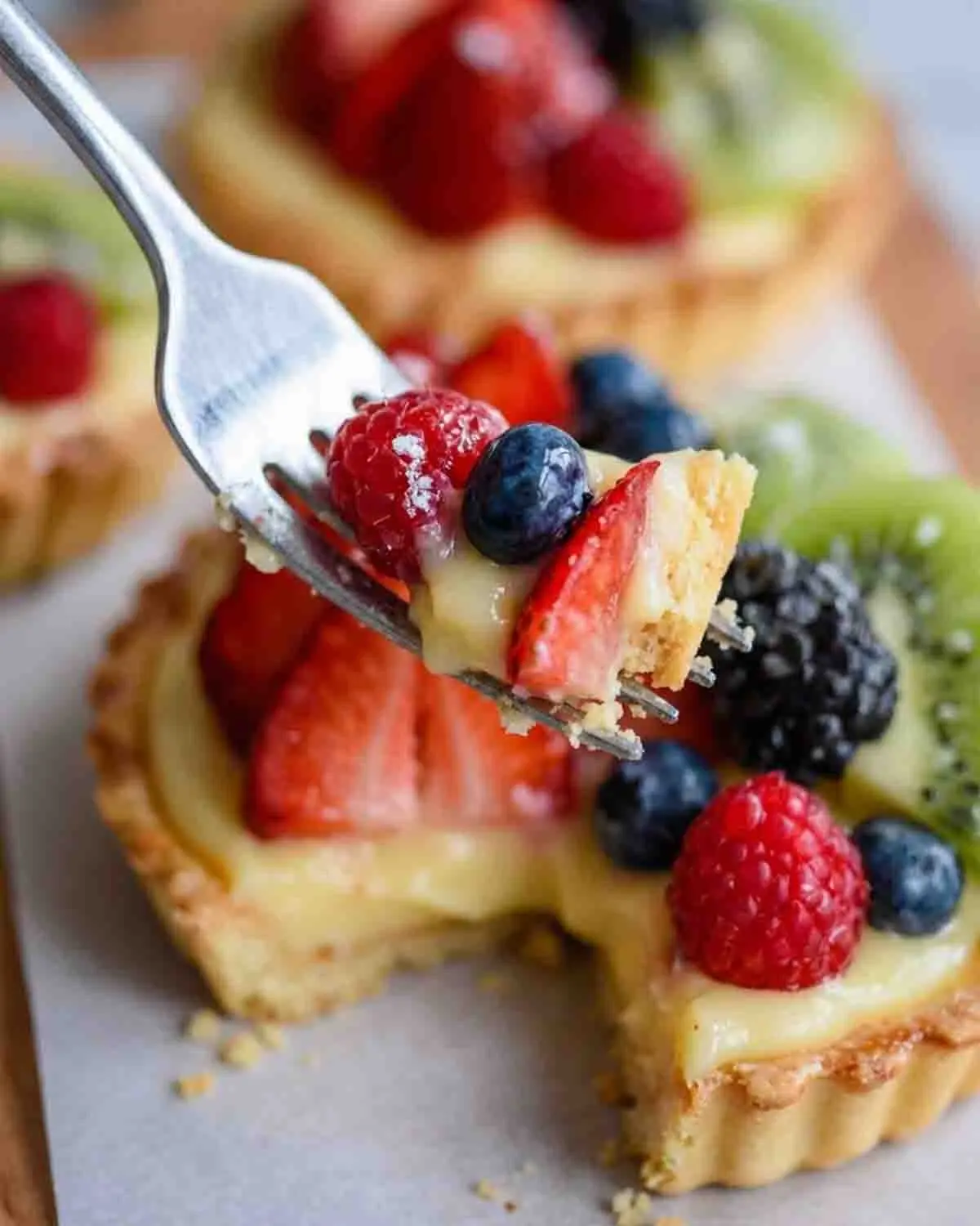 Fruit Tart with Pastry Cream 4 Close-up of fruit tart with pastry cream on a fork topped with strawberries, blueberries, and raspberries over a buttery crust