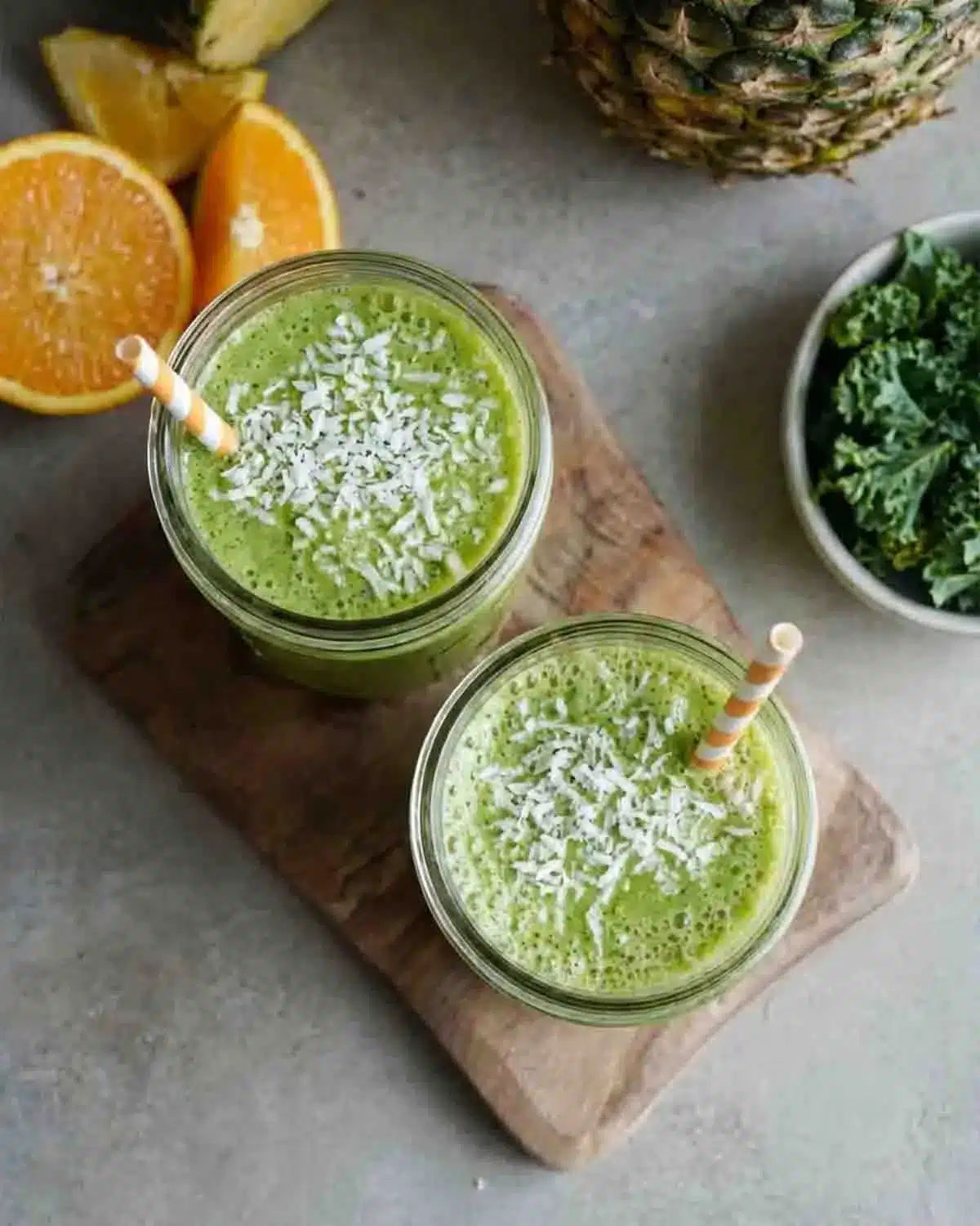 Green Pineapple Coconut Smoothie 4 Top view of Green Pineapple Coconut Smoothie in mason jars topped with shredded coconut, surrounded by pineapple, orange slices, and fresh kale