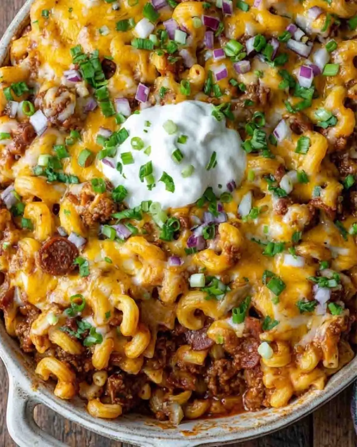 Loaded Chili Cheese Dog Pasta Bake 3 Loaded chili cheese dog pasta bake with melted cheese and hot dog slices served in a cozy home kitchen setting with shelves and glassware in the background.