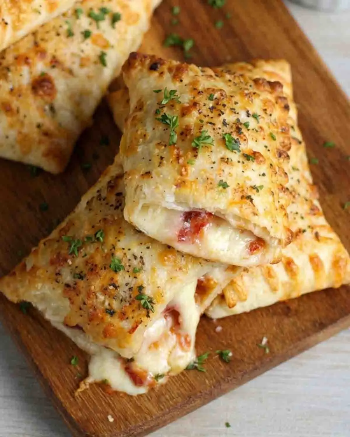 Pizza Pockets Recipe 4 Close-up of crispy baked pizza pockets with melted cheese and pepperoni filling, topped with herbs and served with marinara sauce