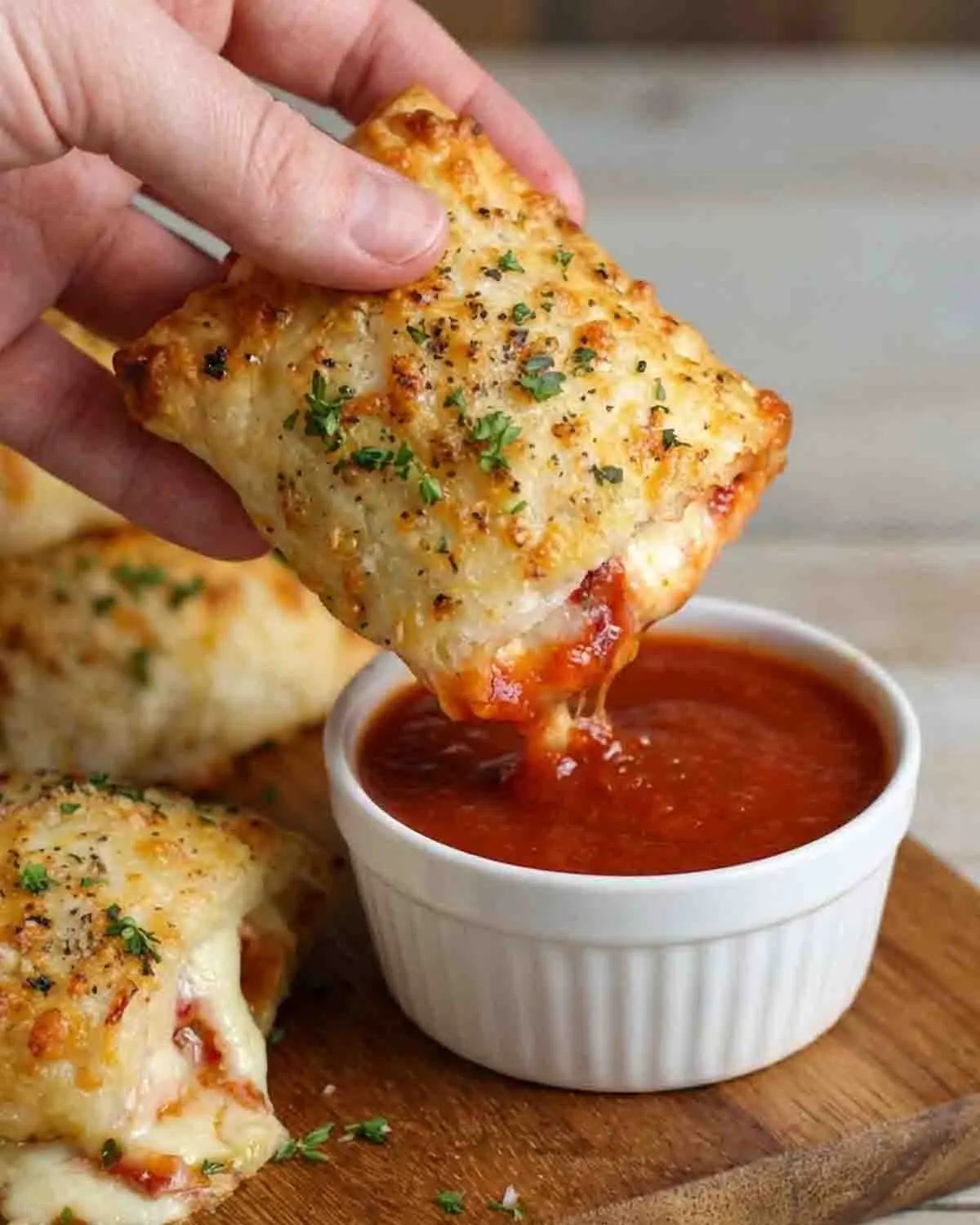 Pizza Pockets Recipe 3 Hand dipping crispy homemade pizza pocket with melted cheese and pepperoni into marinara sauce, golden baked snack on wooden board
