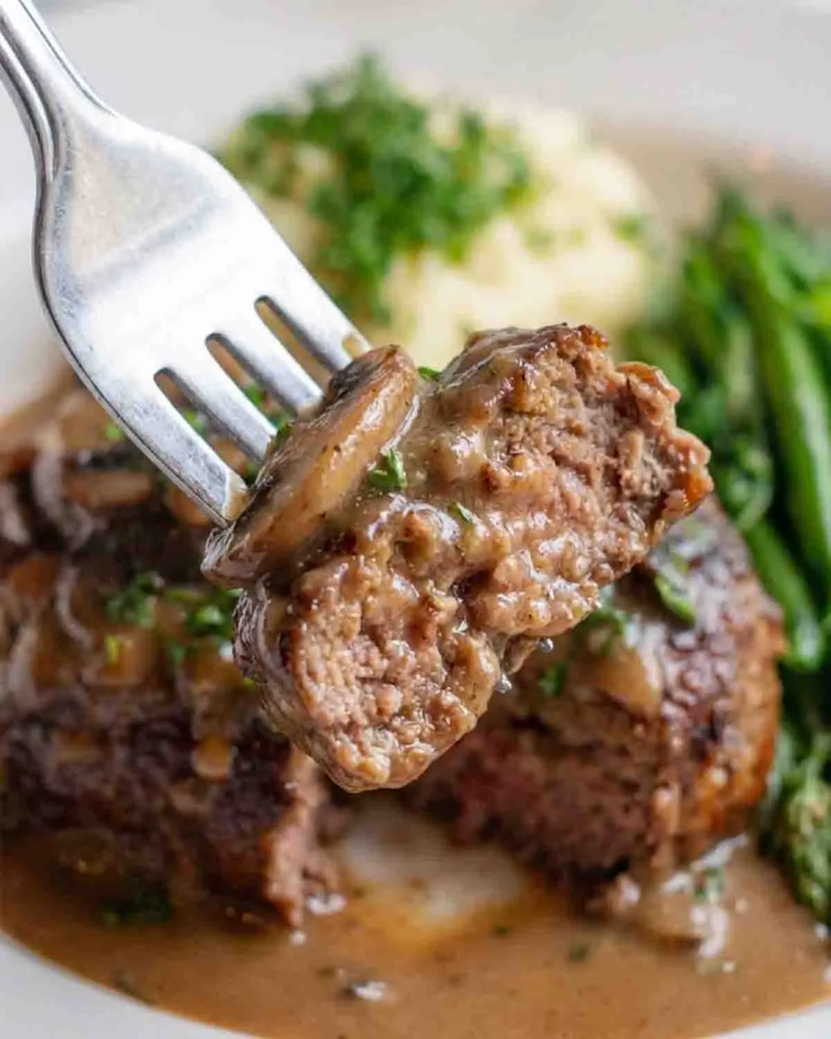 Salisbury Steak Recipe 4 Close-up of Salisbury steak with mushroom onion gravy on a fork served with mashed potatoes and green beans