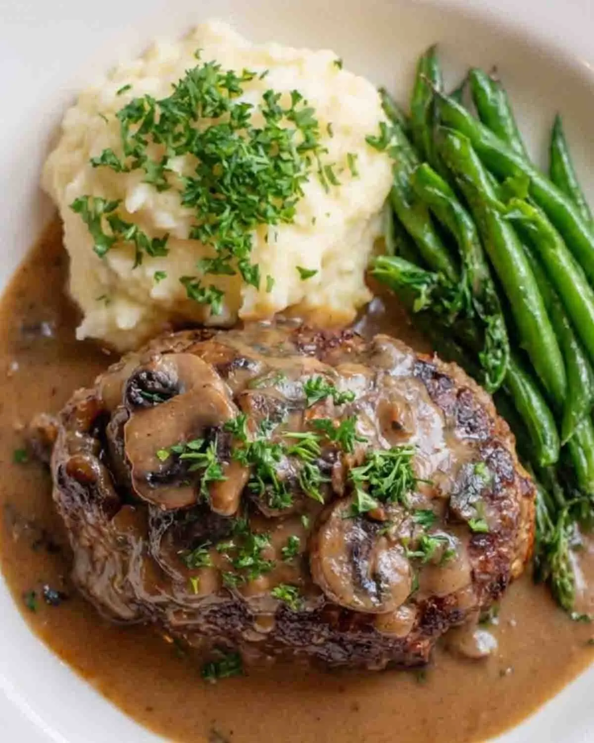 Salisbury Steak Recipe 3 Salisbury steak with mushroom onion gravy served with mashed potatoes and green beans on a plate
