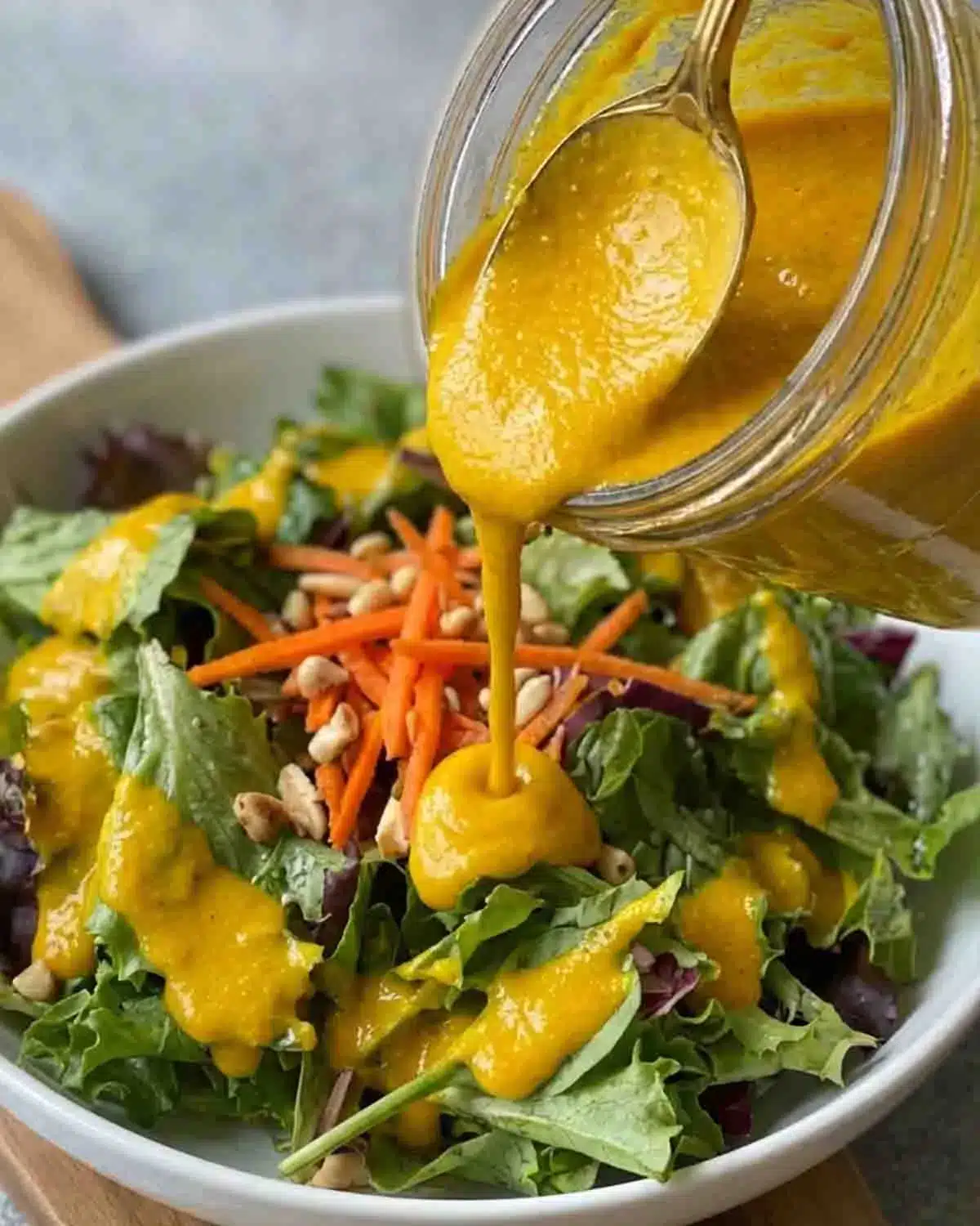 Carrot Ginger Dressing 3 Carrot ginger dressing being poured over a fresh green salad with carrots and seeds