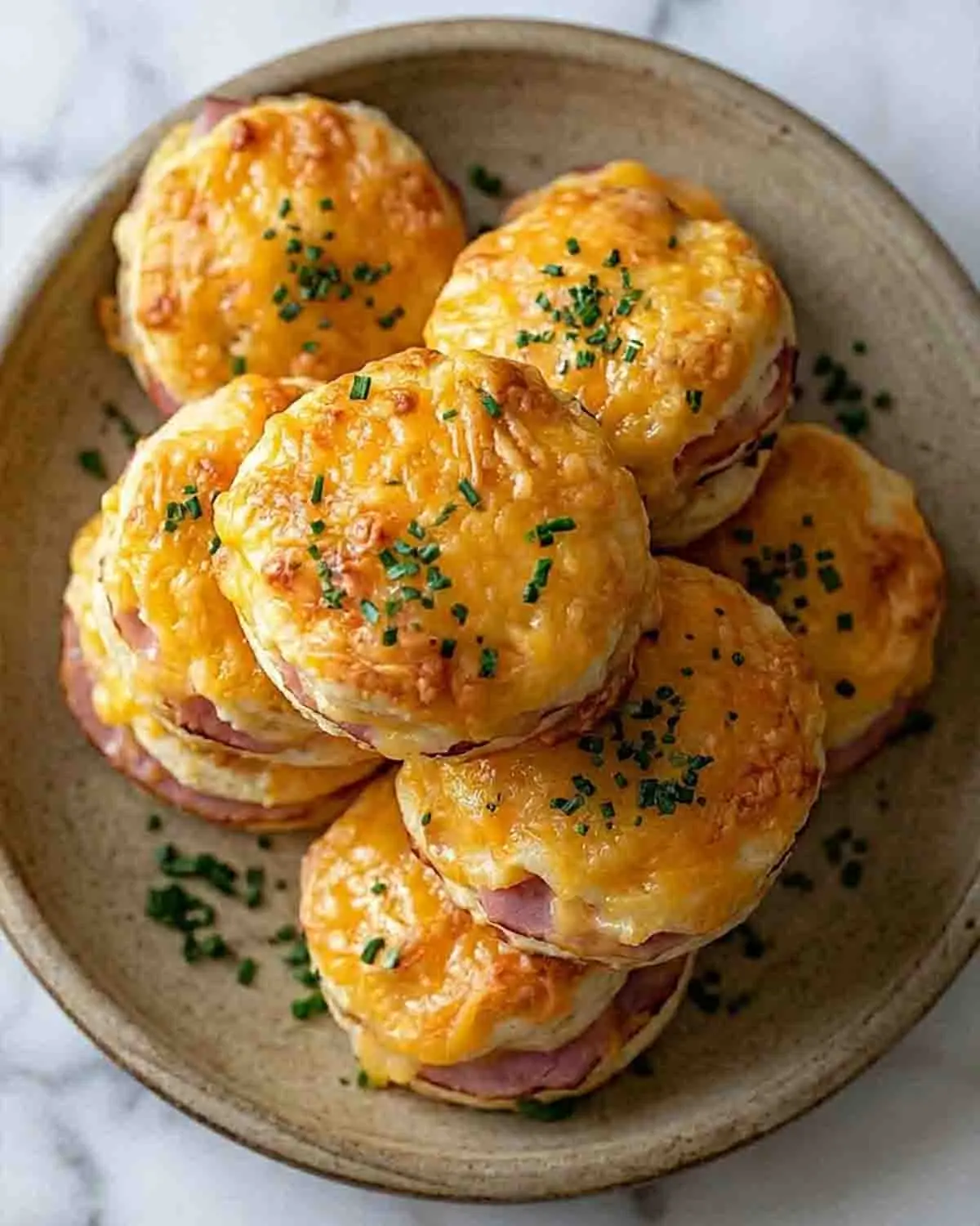 Ham and Cheese Butter Swim Biscuits Recipe 3 Golden ham and cheese butter swim biscuits stacked on a plate with melted cheddar and flaky layers, garnished with fresh herbs