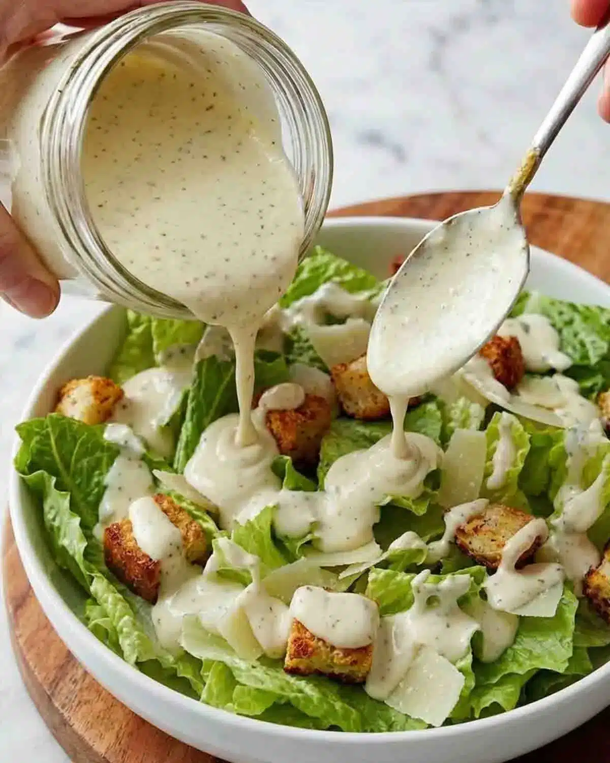 Vegan Caesar Dressing 3 Vegan Caesar dressing being poured over romaine lettuce salad with croutons and dairy-free parmesan